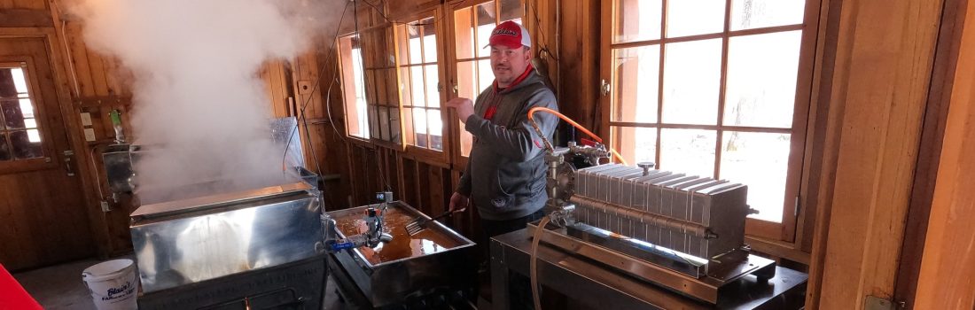 A Wisconsin maple syrup producer stands next to his evaporator and filter press.